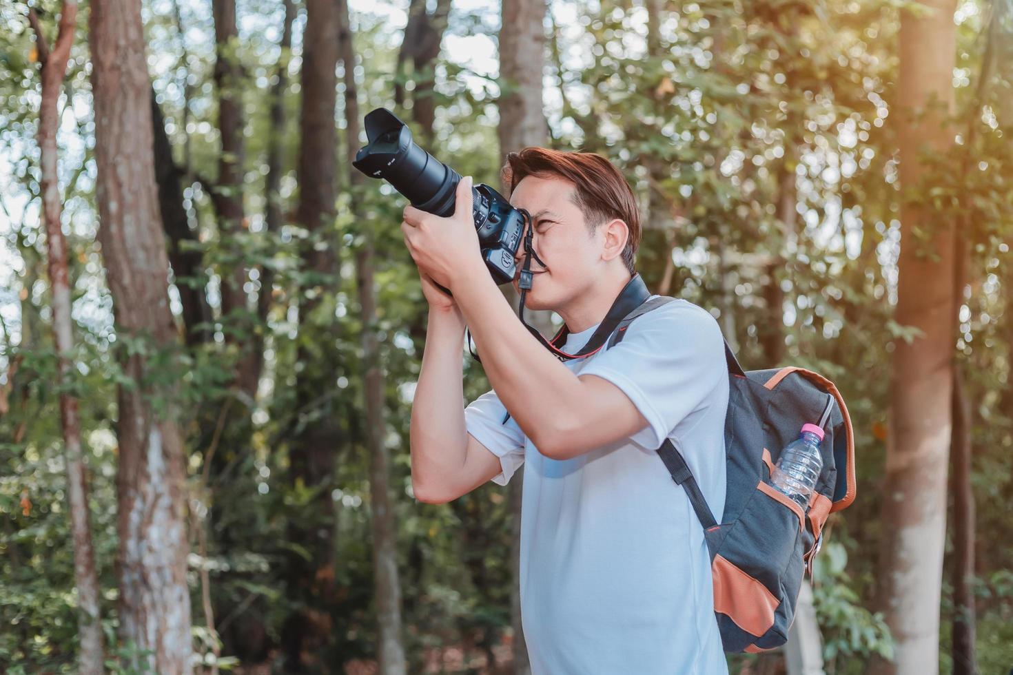 un turista masculino que lleva un bolso, una botella de agua y una cámara camina por el bosque. foto