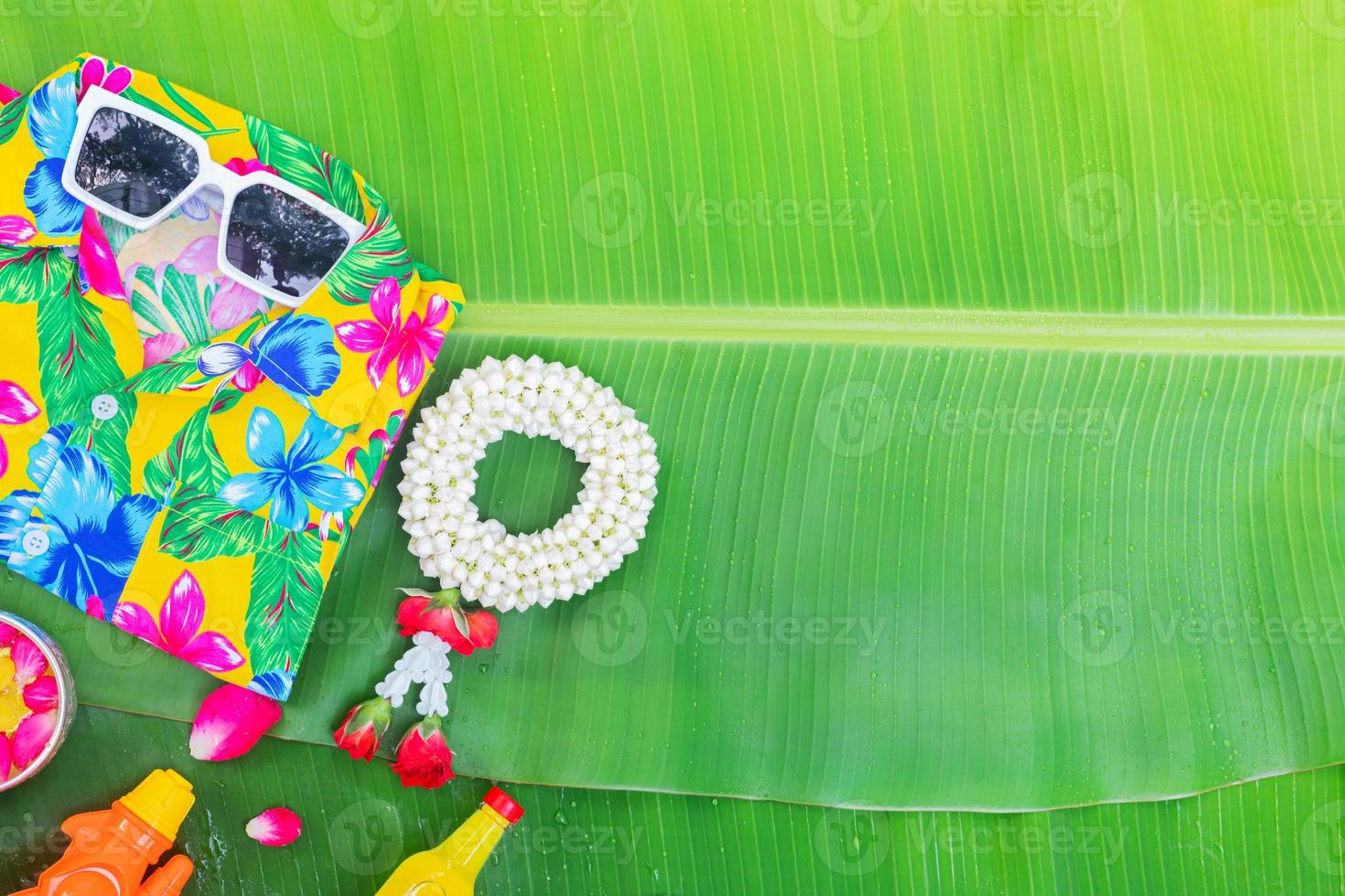 Songkran Festival background with jasmine garland Flowers in a bowl of water, perfume and limestone on a green wet banana leaf background. photo