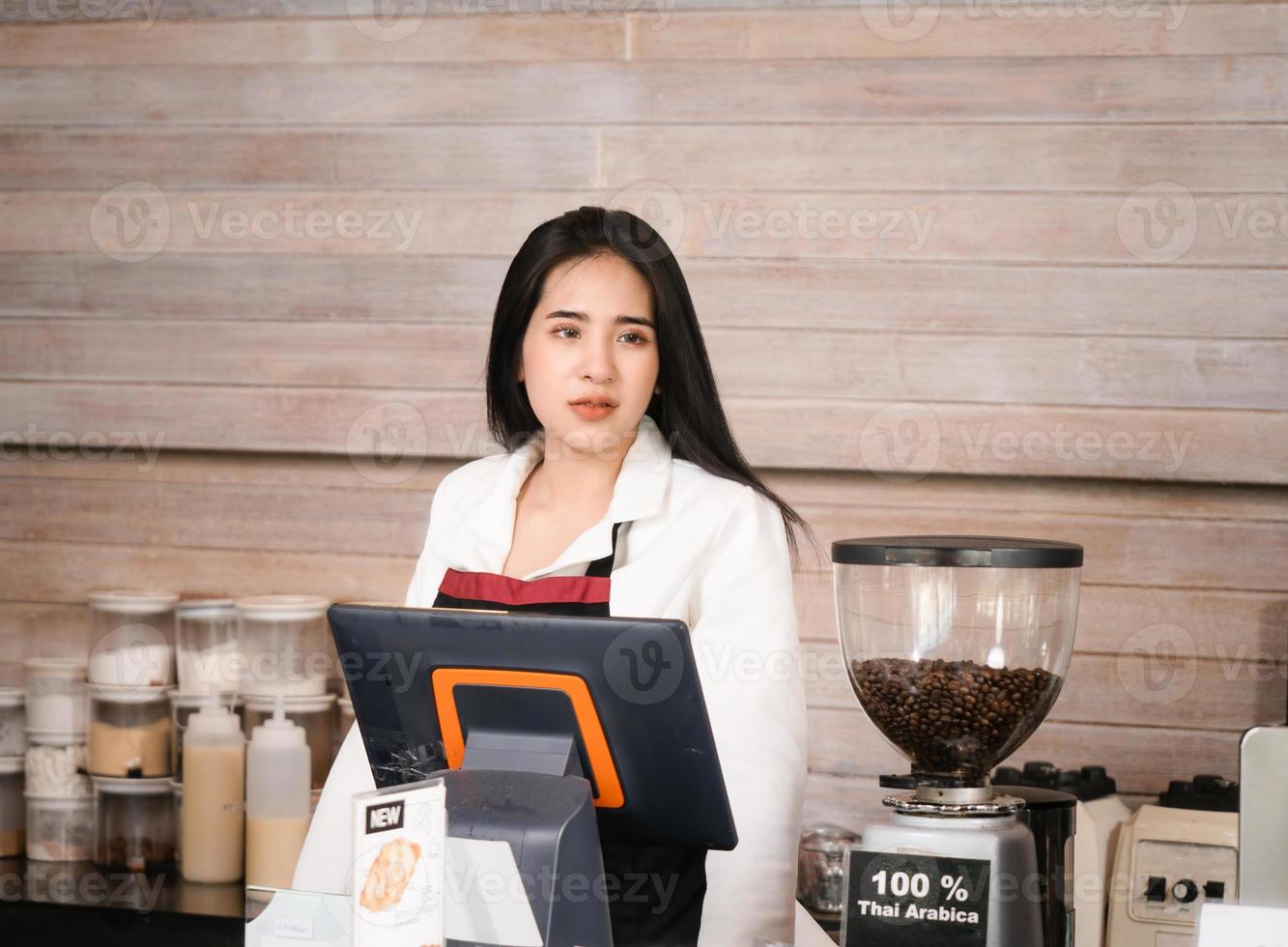 bella mujer asiática propietaria de una cafetería y una barista parada en el bar y revisando los pedidos de los clientes en línea desde una computadora en la cafetería foto