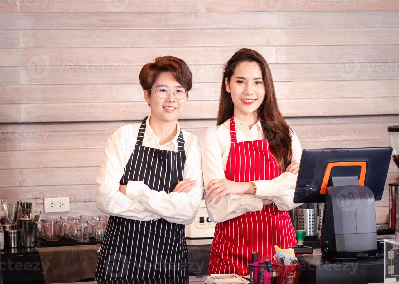 joven pareja lesbiana asiática segura de sí misma que posee una cafetería y un barista parado en el bar y esperando pedidos de clientes desde una computadora en la cafetería foto