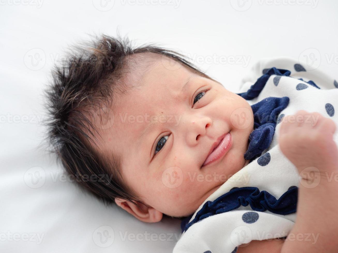 retrato de un bebé o bebé recién nacido asiático australiano de tres semanas acostado en la cama blanca y abriendo los ojos. foto