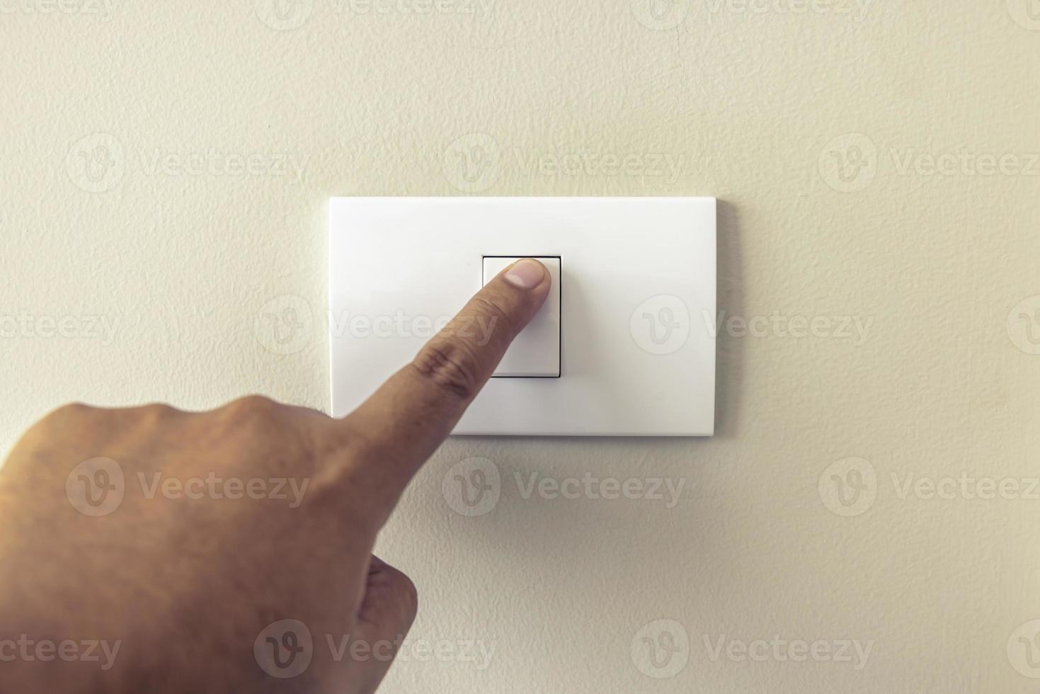 Close up Man's fingers are turning on or off a white light switch on a cream colored wall at night at home. Energy, safety, save electricity, copy space photo