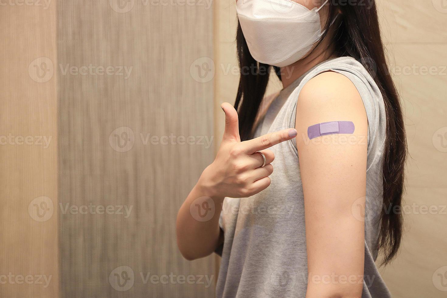 Healthy asian woman concept of recommended inoculation,  Woman holding down her shirt sleeve and showing her arm with bandage after receiving vaccination. photo