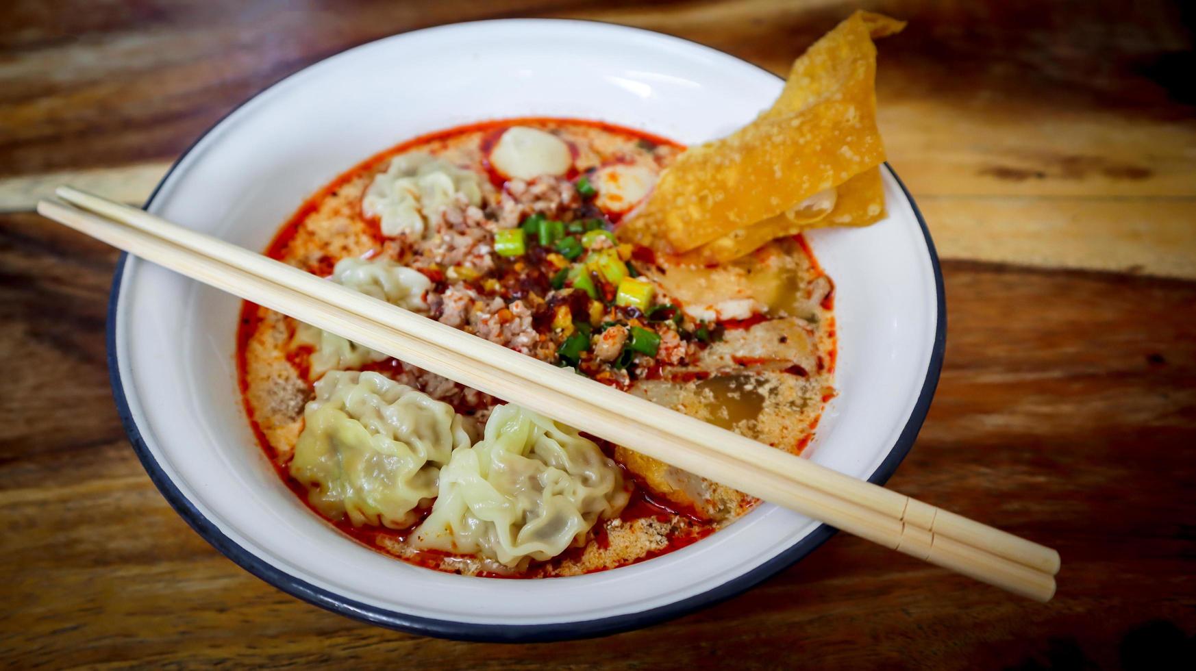 Pork wonton in spicy Tom Yum soup with minced pork and fish ball in white bowl. photo