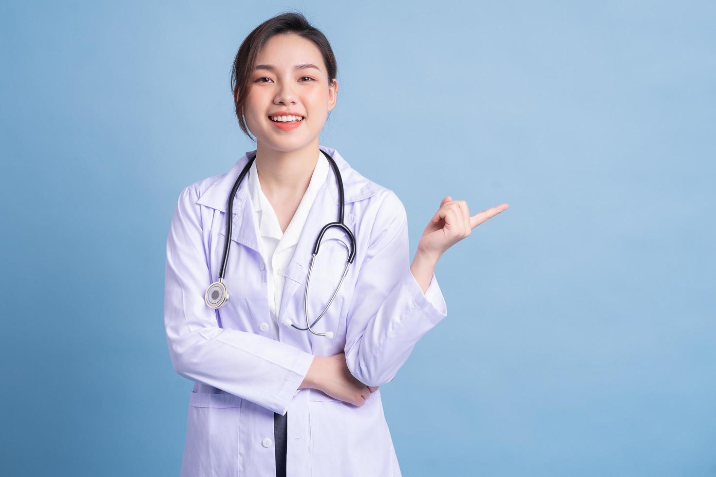 joven doctora asiática de pie sobre fondo azul foto