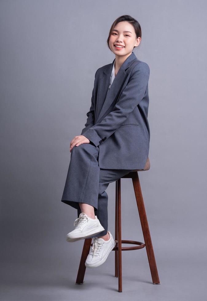 Young Asian businesswoman sitting on chair and posing on gray background photo
