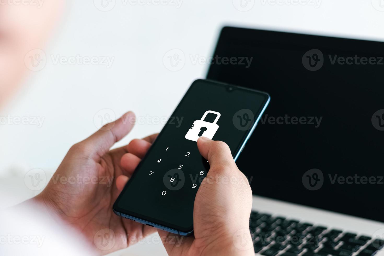 Hacking a Phishing mobile phone with a password to access a smartphone, security threats online, and fraud. A young man with a cell phone and laptop is secure in his bank account. photo