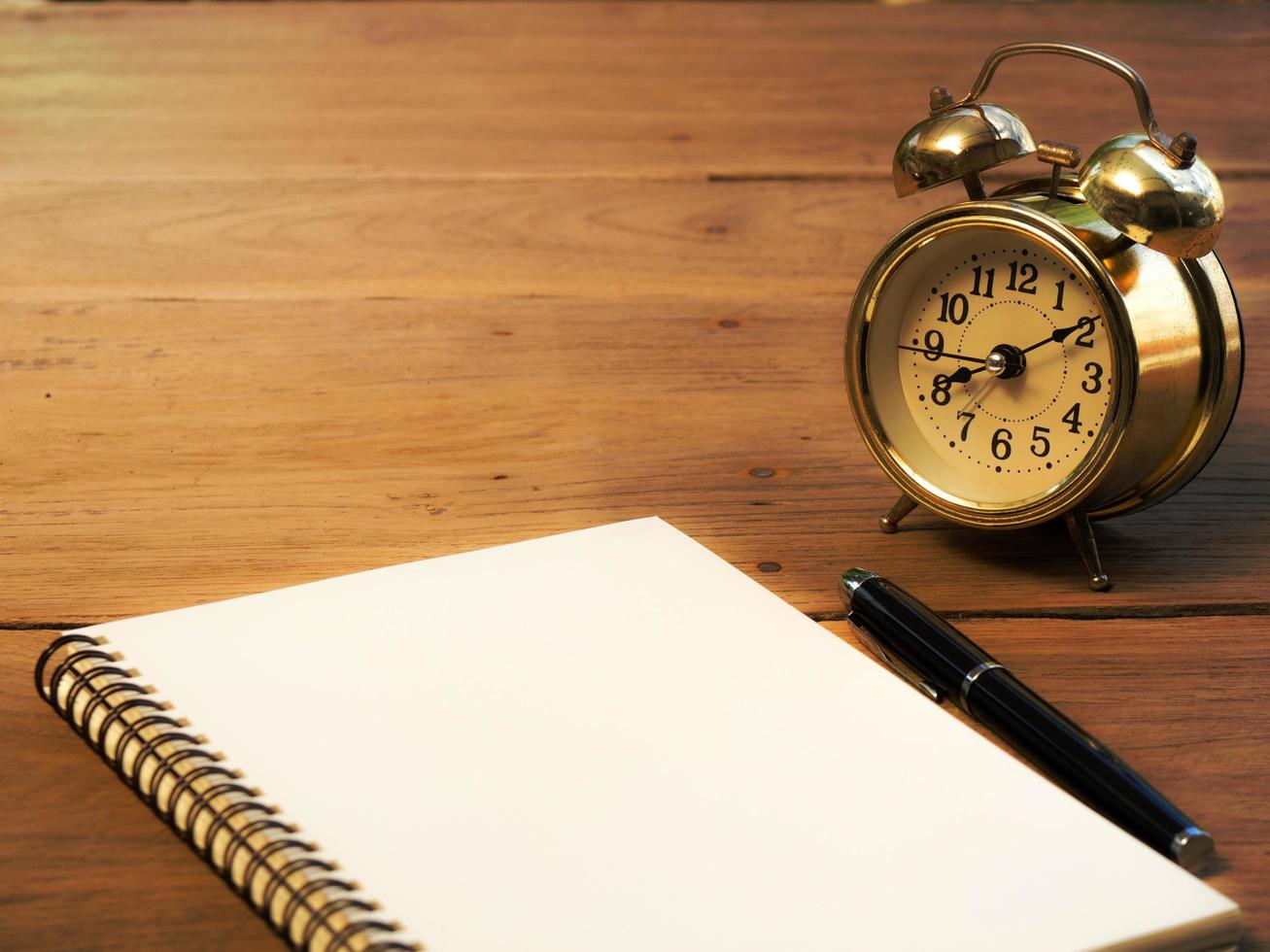 Blank notebook with vintage alarm clock and black pen on wood table photo