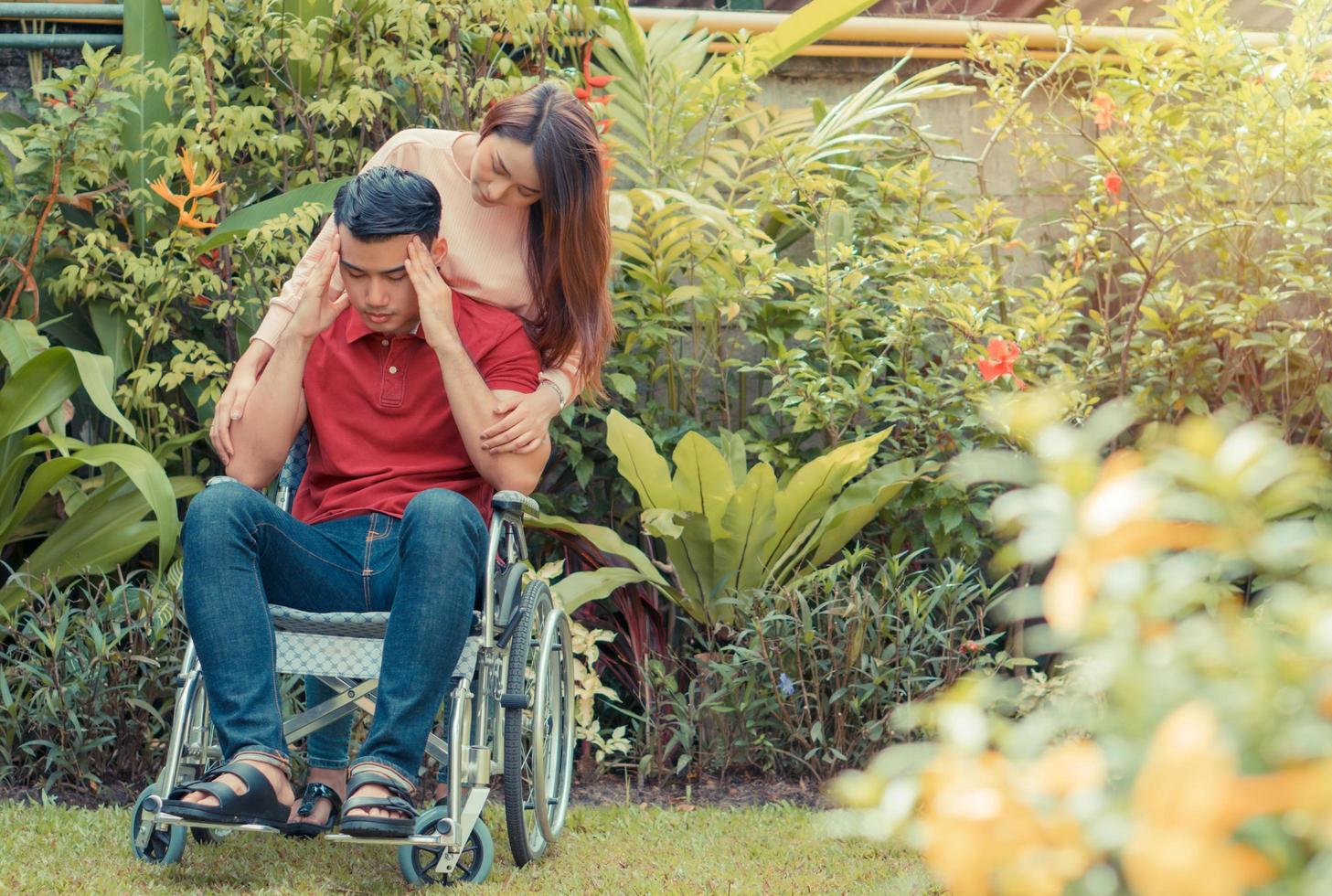 hombre asiático en silla de ruedas e infeliz y doloroso. una mujer de pie detrás de la silla de ruedas y está animando a su marido, cuyos pies le duelen la pierna debido a un accidente. concepto de cuidado y apoyo foto