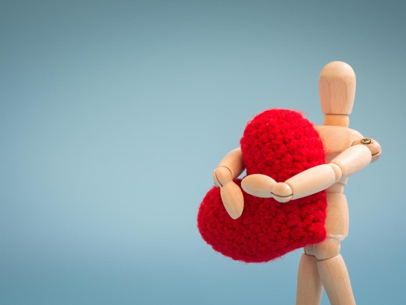 Wooden puppet standing and holding a red heart on the blue screen background. Wooden puppet holding the heart with love and care. Concept of take care and love. photo