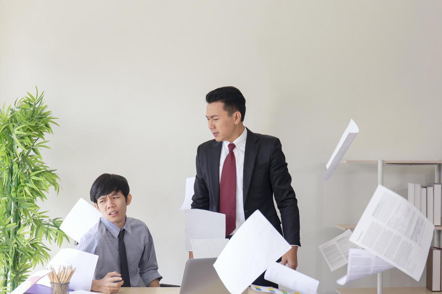 An angry Asian manager, his employees unable to work as expected, throwing paper in the office. photo