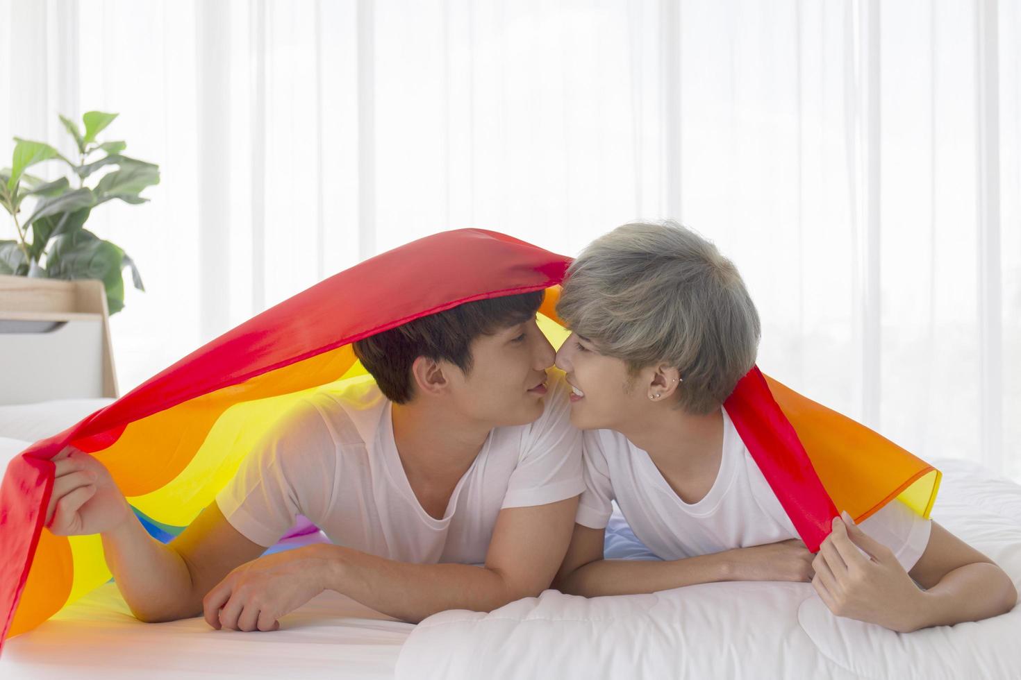 Male and Asian couples lay on their heads a multicolored flag bearing LGBT signs, expressing openly gay men accepting LGBT concepts. photo