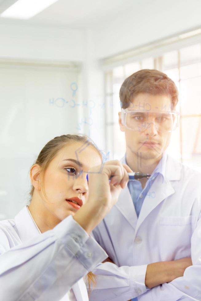 Close-up, a group of scientists, young women and young men are recording formulas on a glass board and have a beautiful orange light. photo