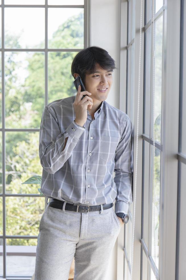 A young Asian businessman stands on the balcony of a window talking on the phone. photo