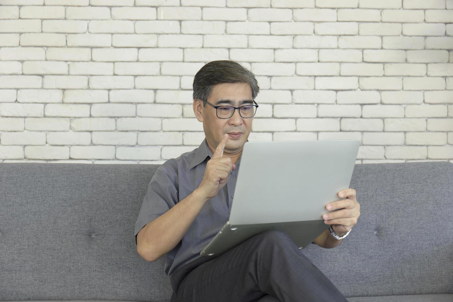 An Asian middle-aged man holding a notebook in his hand is sitting on a sofa taking a video call. photo