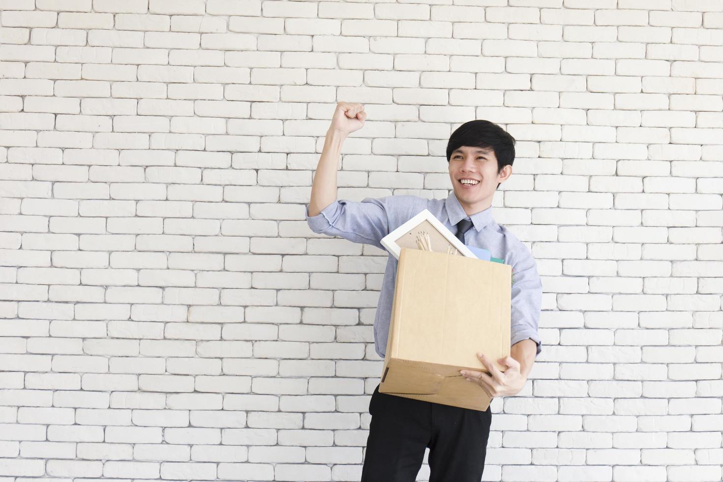 un hombre asiático se regocija en la oficina después de ser despedido, guardando pertenencias personales en cajas de cartón. foto