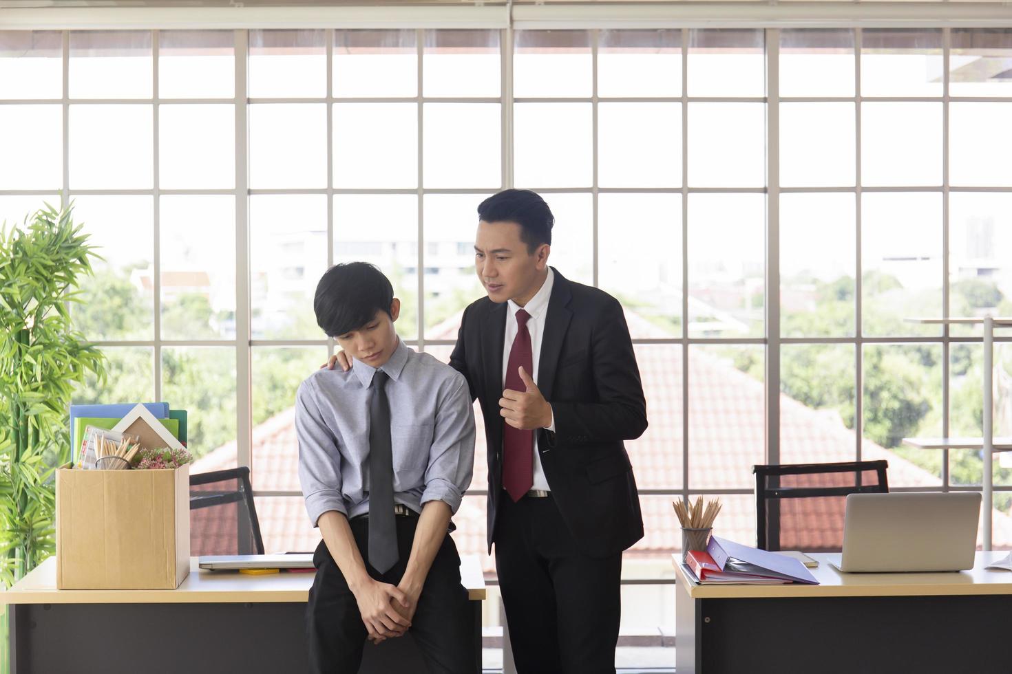 el supervisor se pone de pie para alentar a un subordinado masculino asiático al lado de un escritorio en la oficina. foto