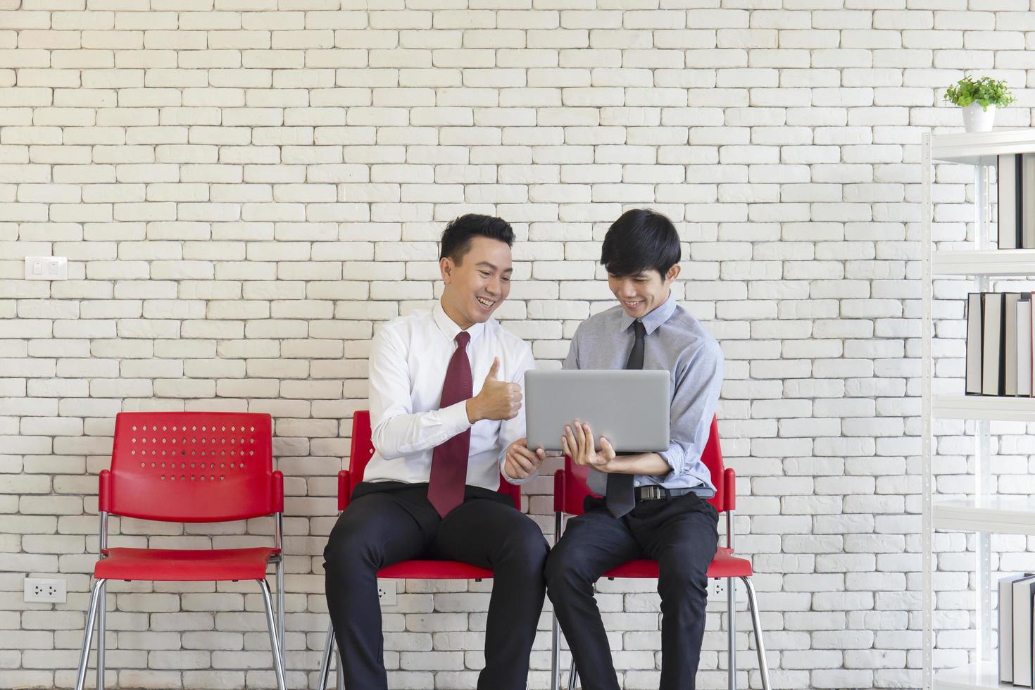 Two Asian men sit on red plastic chairs waiting for a job interview. photo