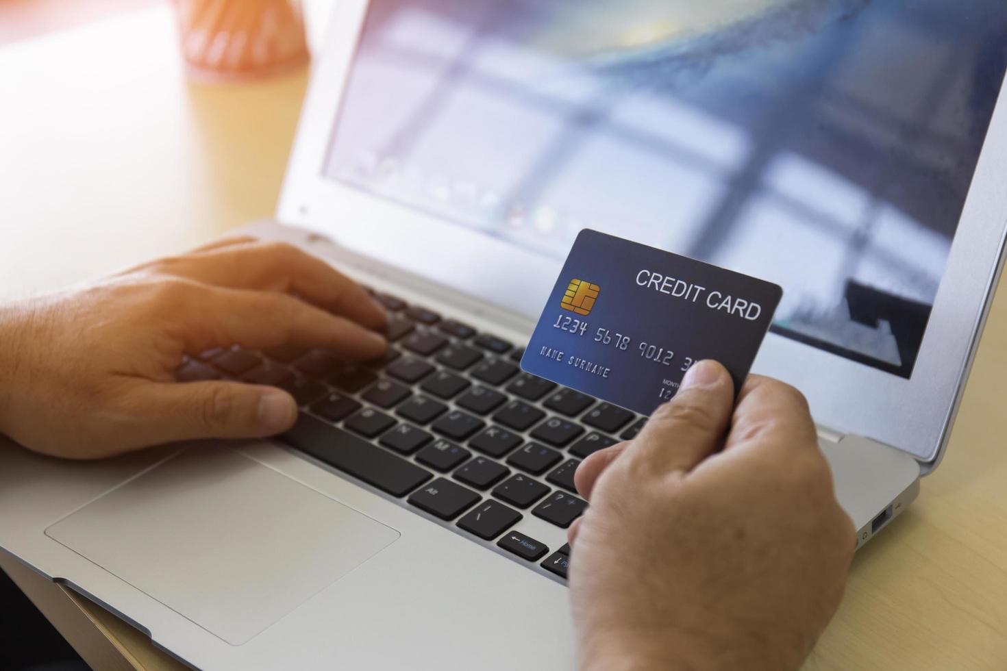 Hand holding credit card and using a laptop. Businessman or entrepreneur working from home. Online shopping, e-commerce, internet banking, spending money, work from home concept. photo