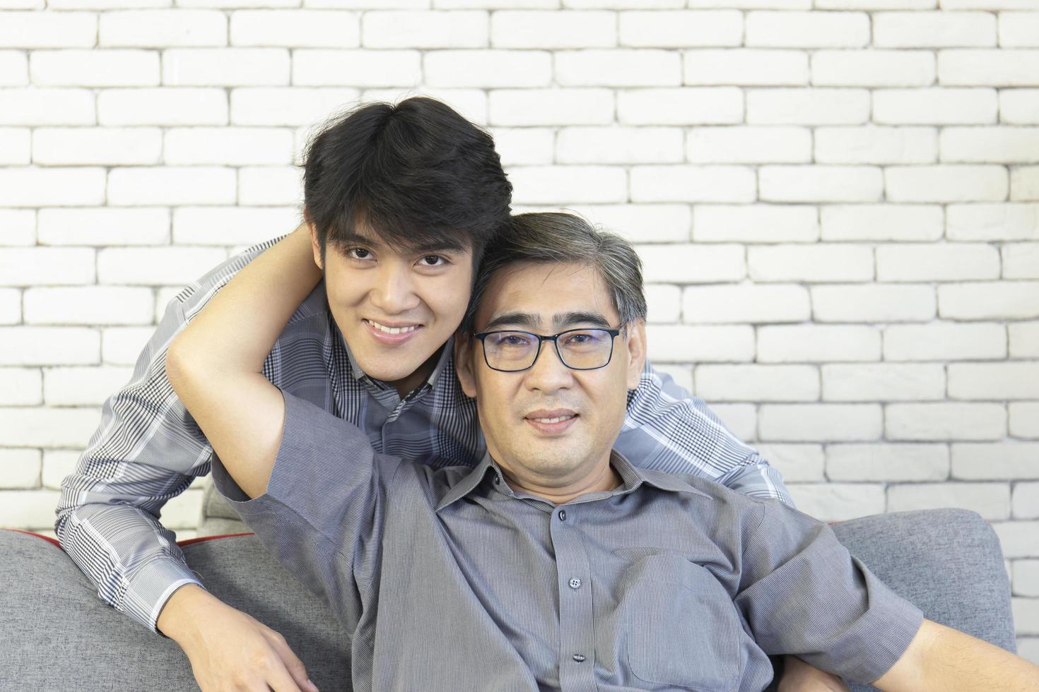 A middle-aged father and an Asian son hugged each other on the sofa with a happy smile. photo