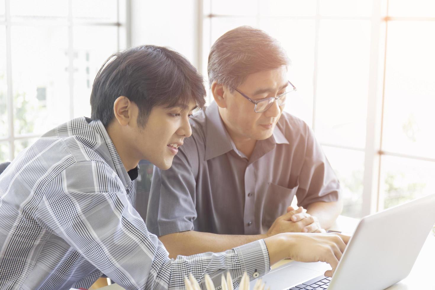 An elderly Asian man is learning how to trade online through the Internet with a young man who teaches him. photo