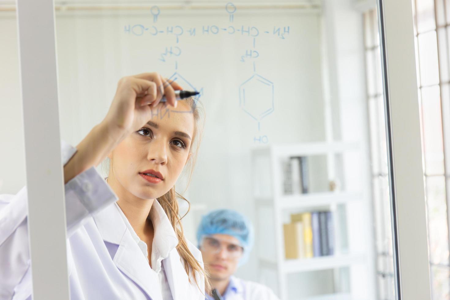 A close-up of a group of young scientists is saving a formula on a glass board. photo