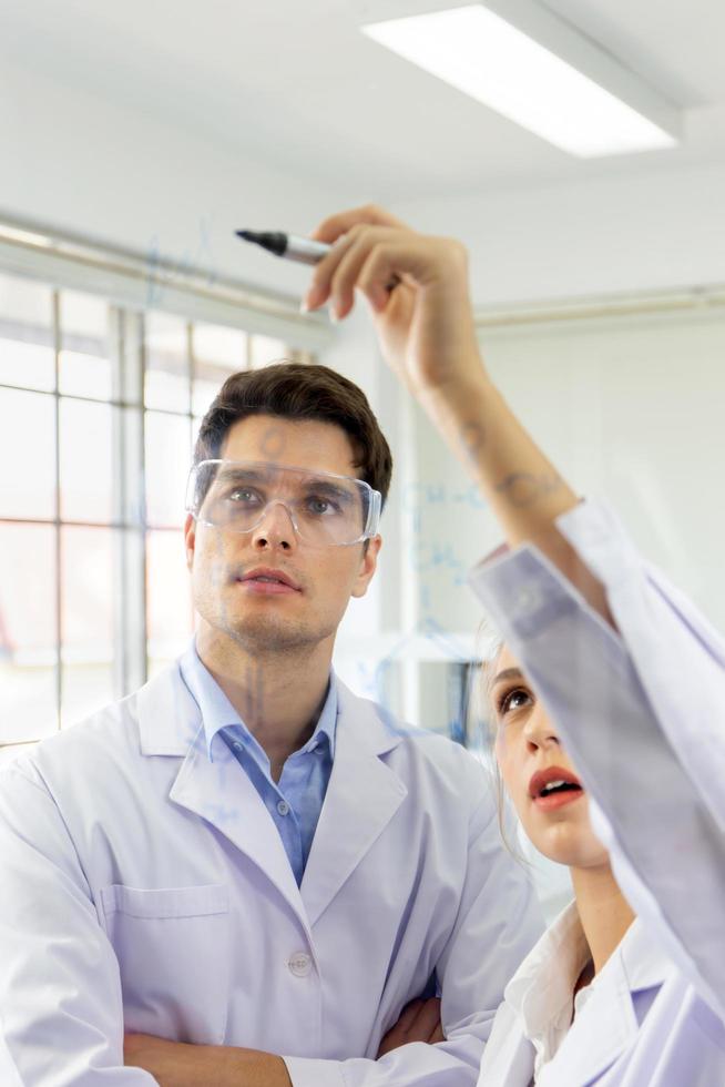 Close-up, a group of scientists, young women and young men are recording formulas on a glass board. photo