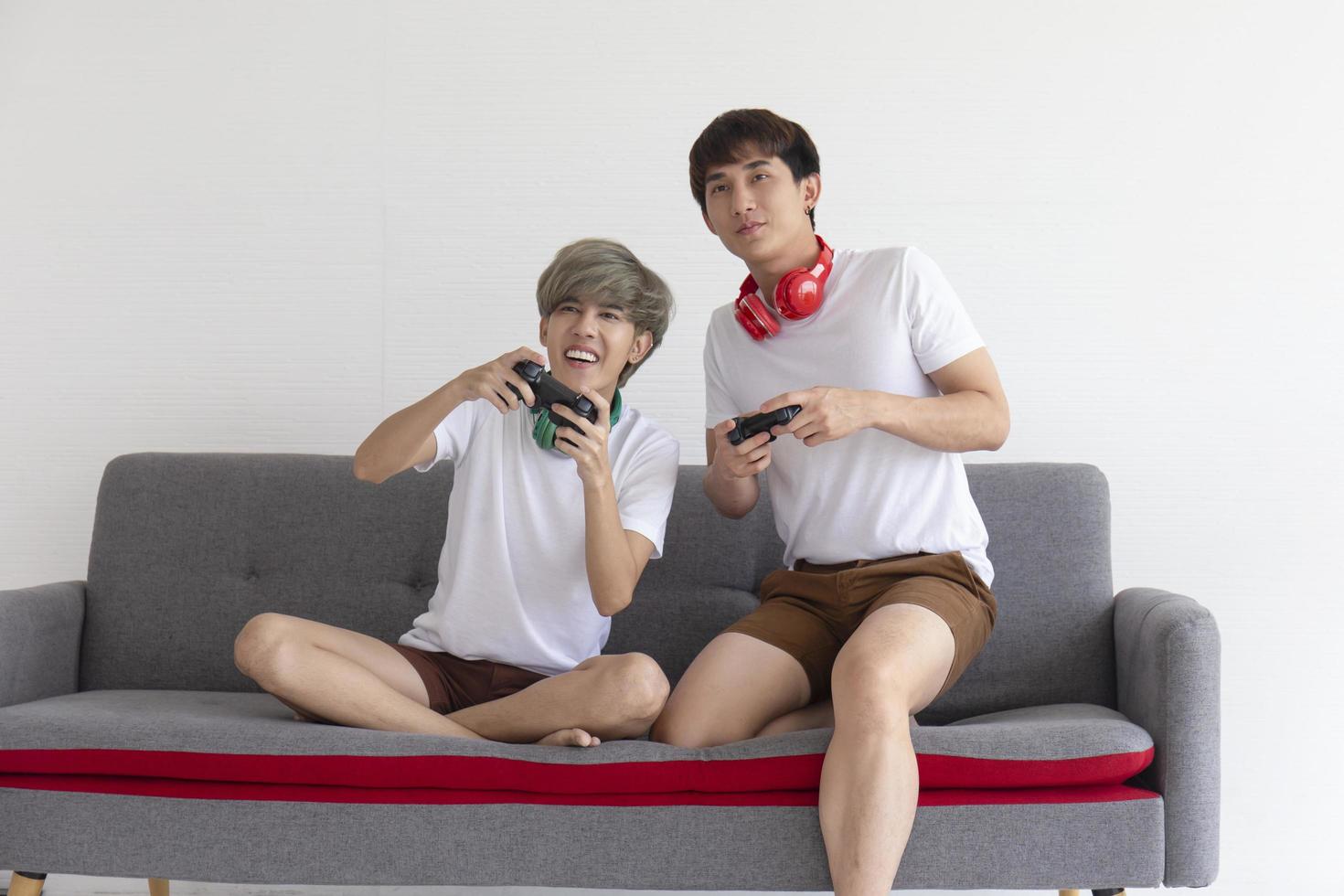 A male couple with an Asian man sitting on a sofa playing video games having fun. photo