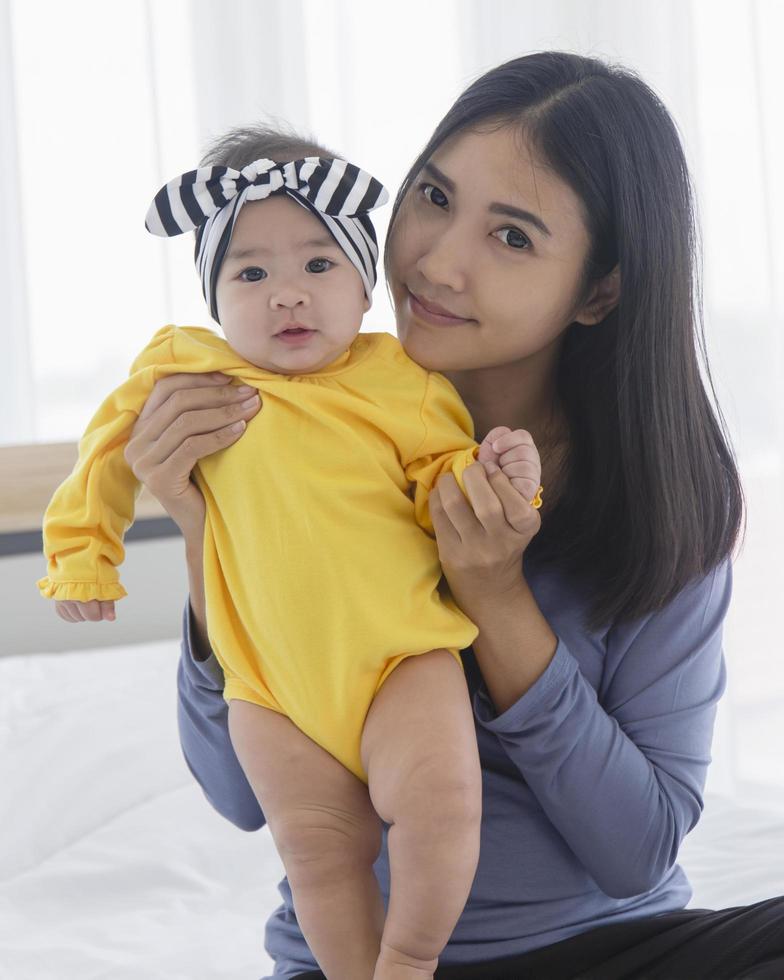 An Asian mom plays with her baby in bed with love and care. photo