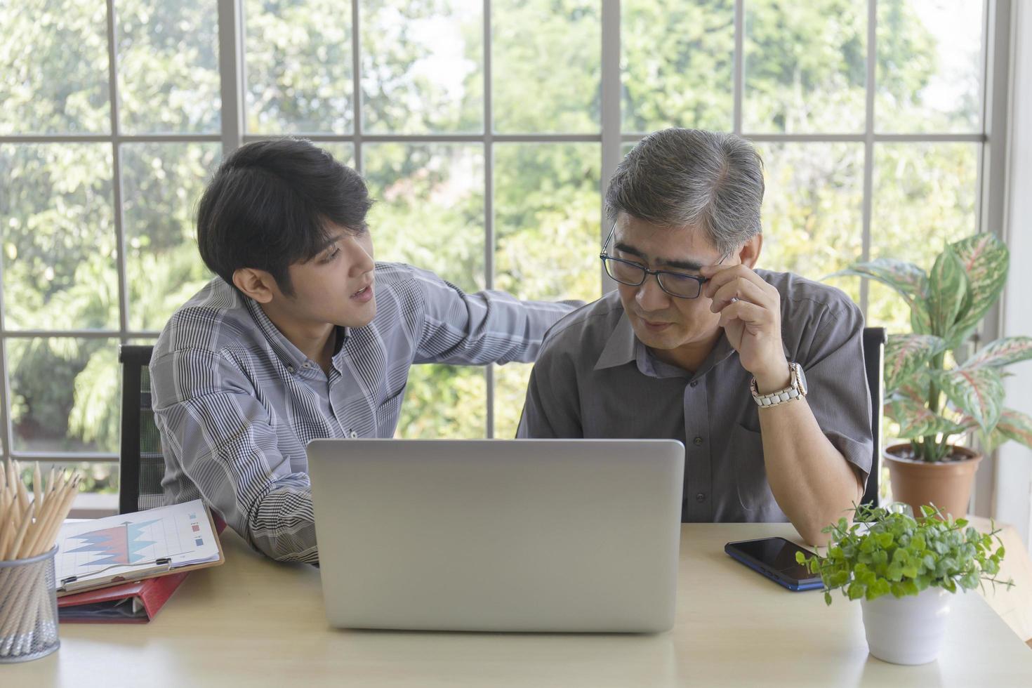 An elderly Asian man is learning how to trade online through the Internet with a young man who teaches him. photo