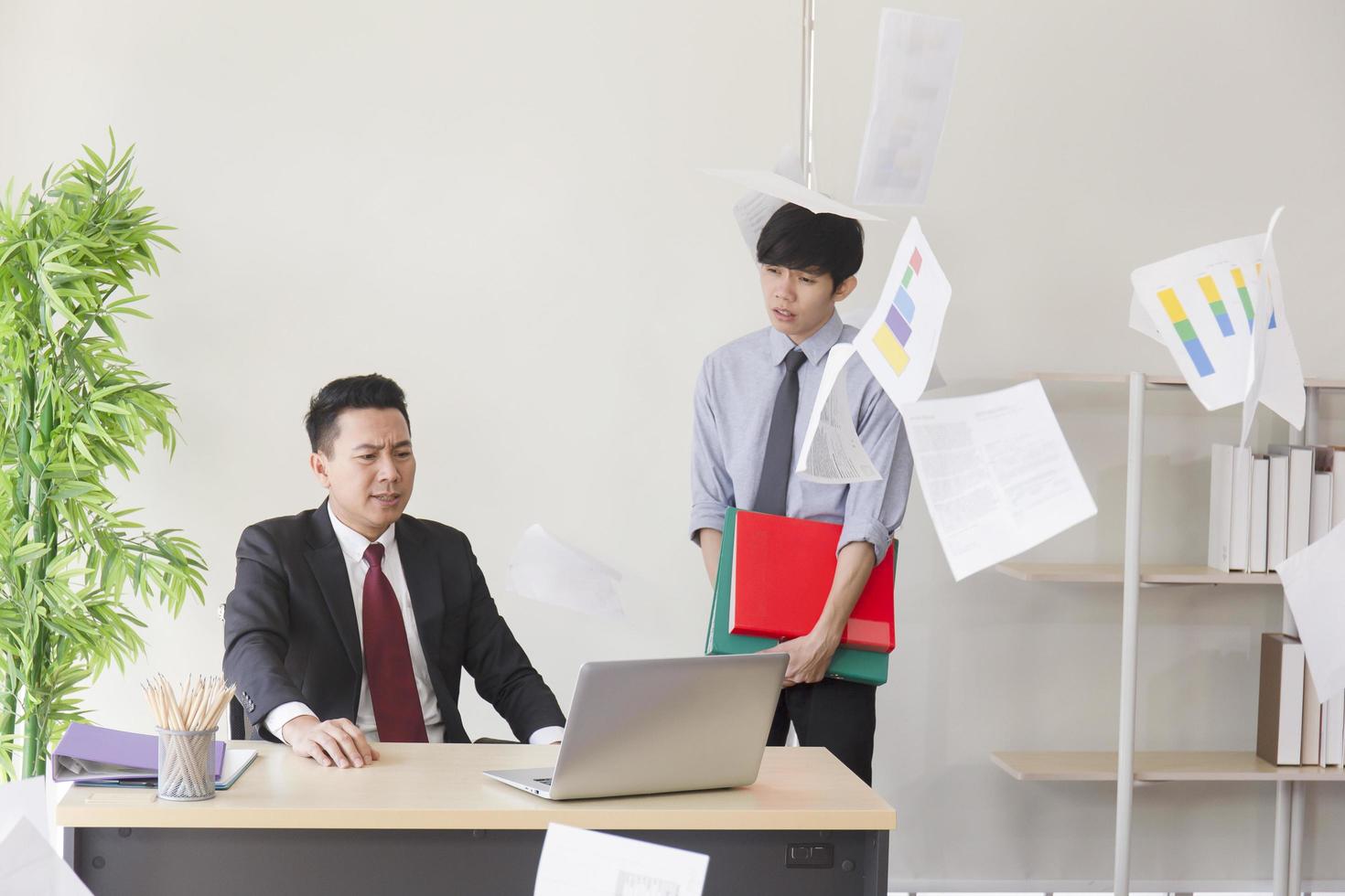 An angry Asian manager, his employees unable to work as expected, throwing paper in the office. photo