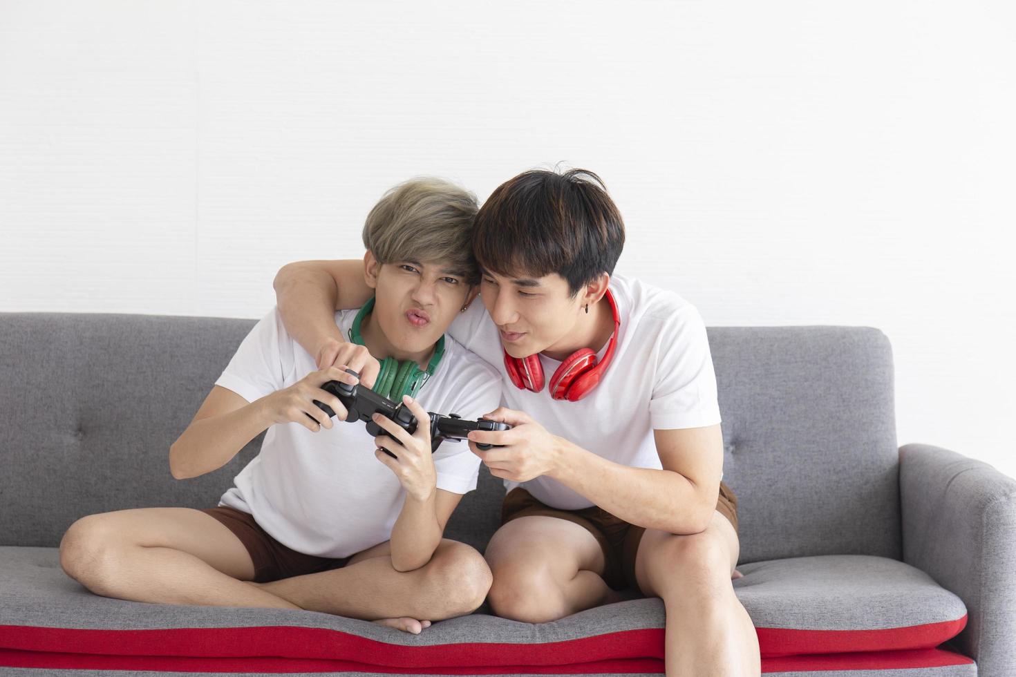 A male couple with an Asian man sitting on a sofa playing video games having fun. photo