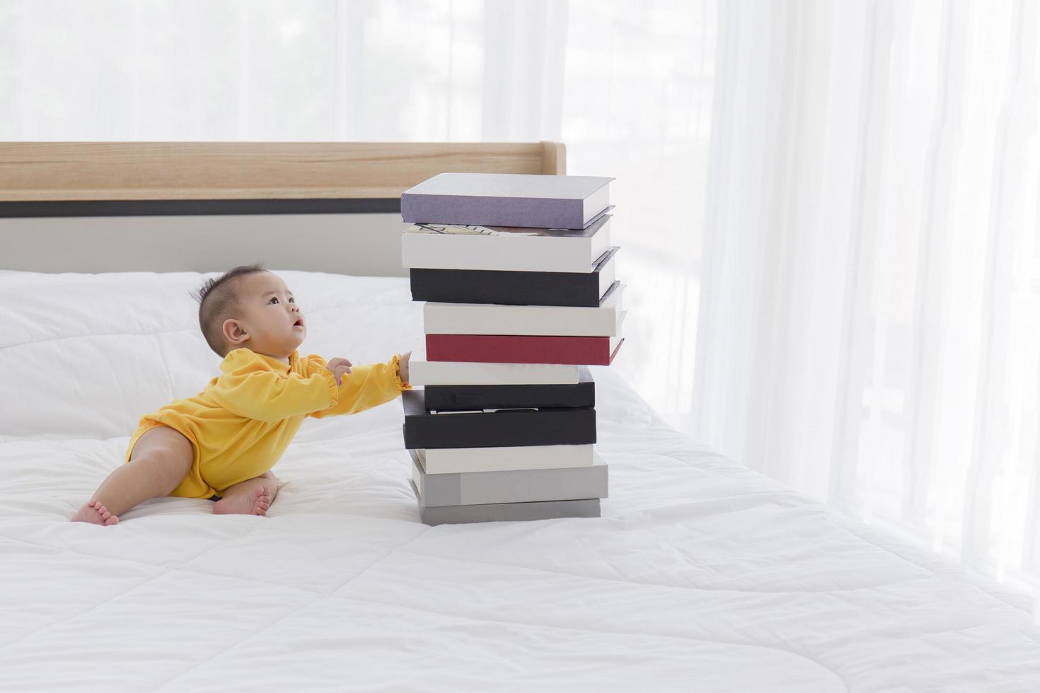 A baby with a pile of books on the bed. photo