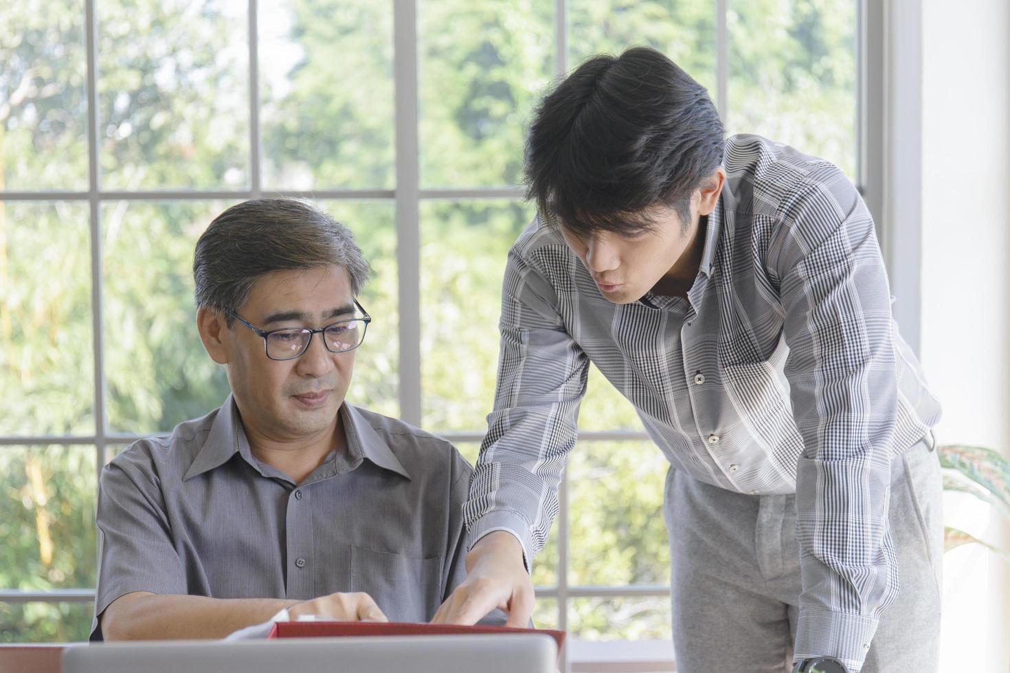 An Asian middle-aged man with his son standing next to a desk in the office. photo