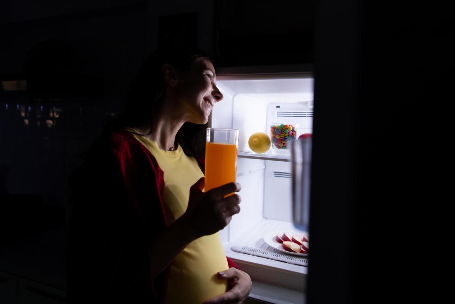 A pregnant woman who wakes up late at night looking for food in the refrigerator photo