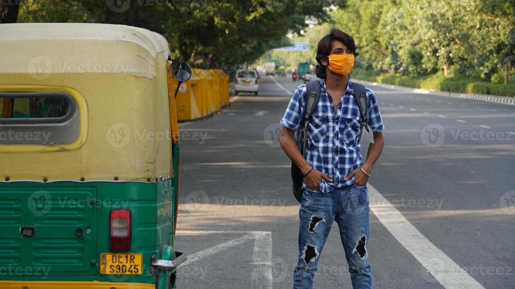 a boy at bus stand wearing mask in road behind auto photo