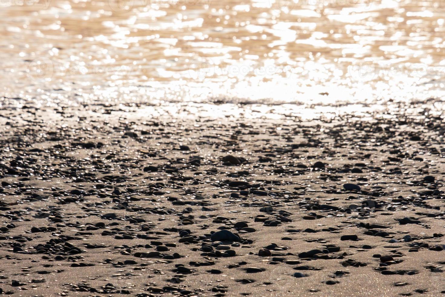 Beach pebbles and sea foam in contrasting afternoon light on a beach in Cyprus. Suitable as background photo