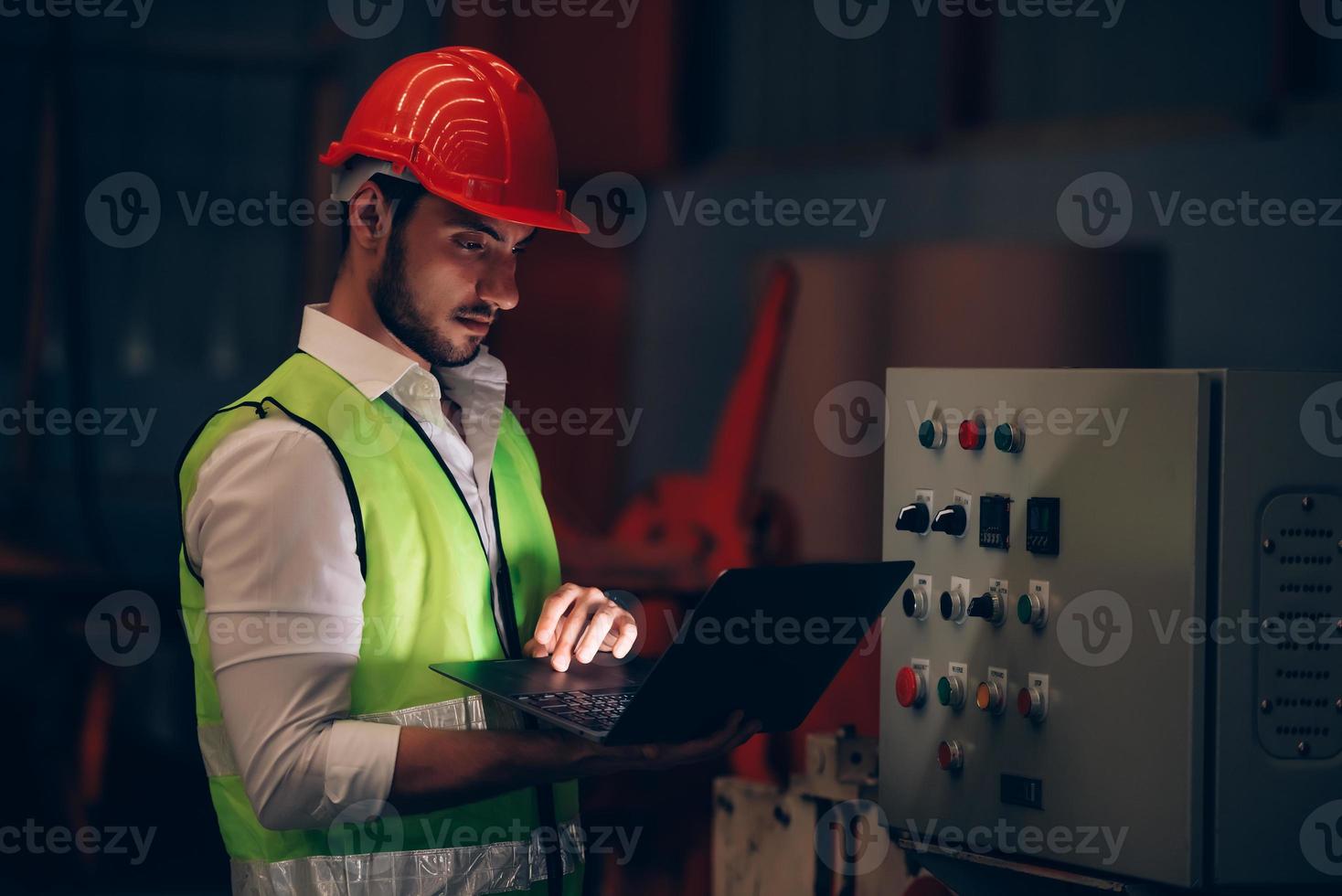 trabajador de fábrica revisando el sistema eléctrico y el proceso de la máquina a través de una computadora portátil en un trabajo de horas extra en el lugar de trabajo industrial foto