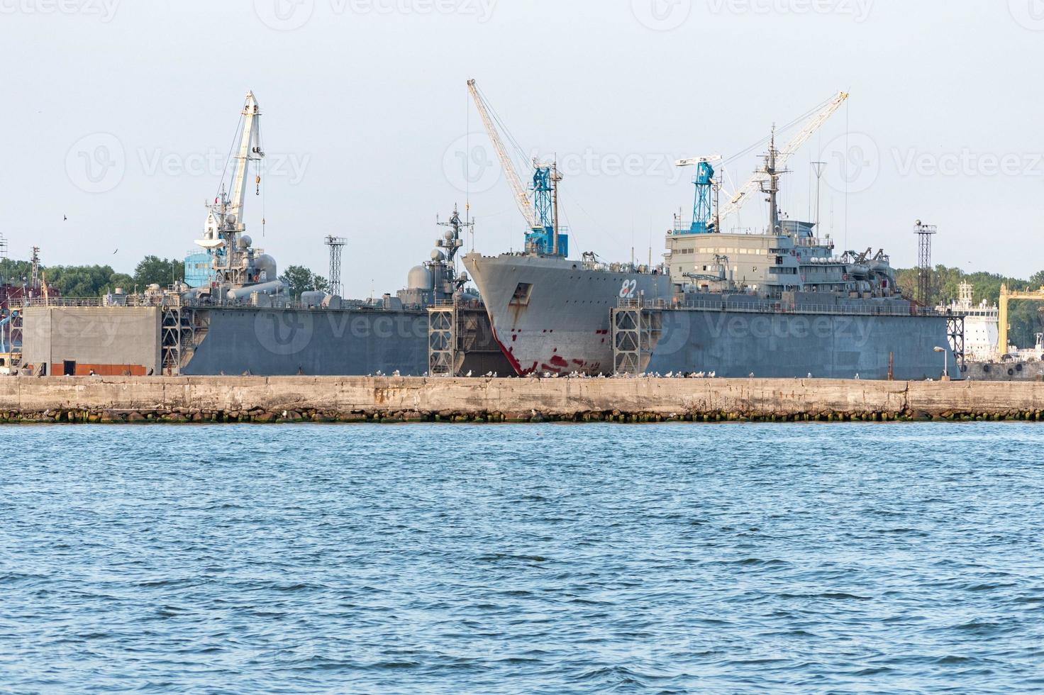 Large iron navy ships in shipyard for repair. Big crane in dockyard. Blue sea harbor photo