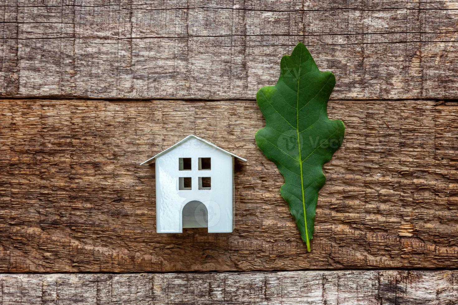 Toy House and green oak leaf on wooden background photo