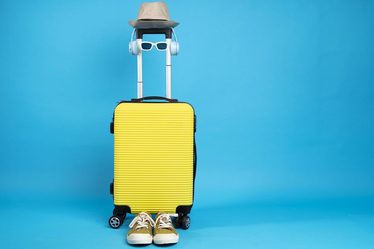 Yellow suitcase with sun glasses, hat and camera on pastel blue background. travel concept. minimal style photo