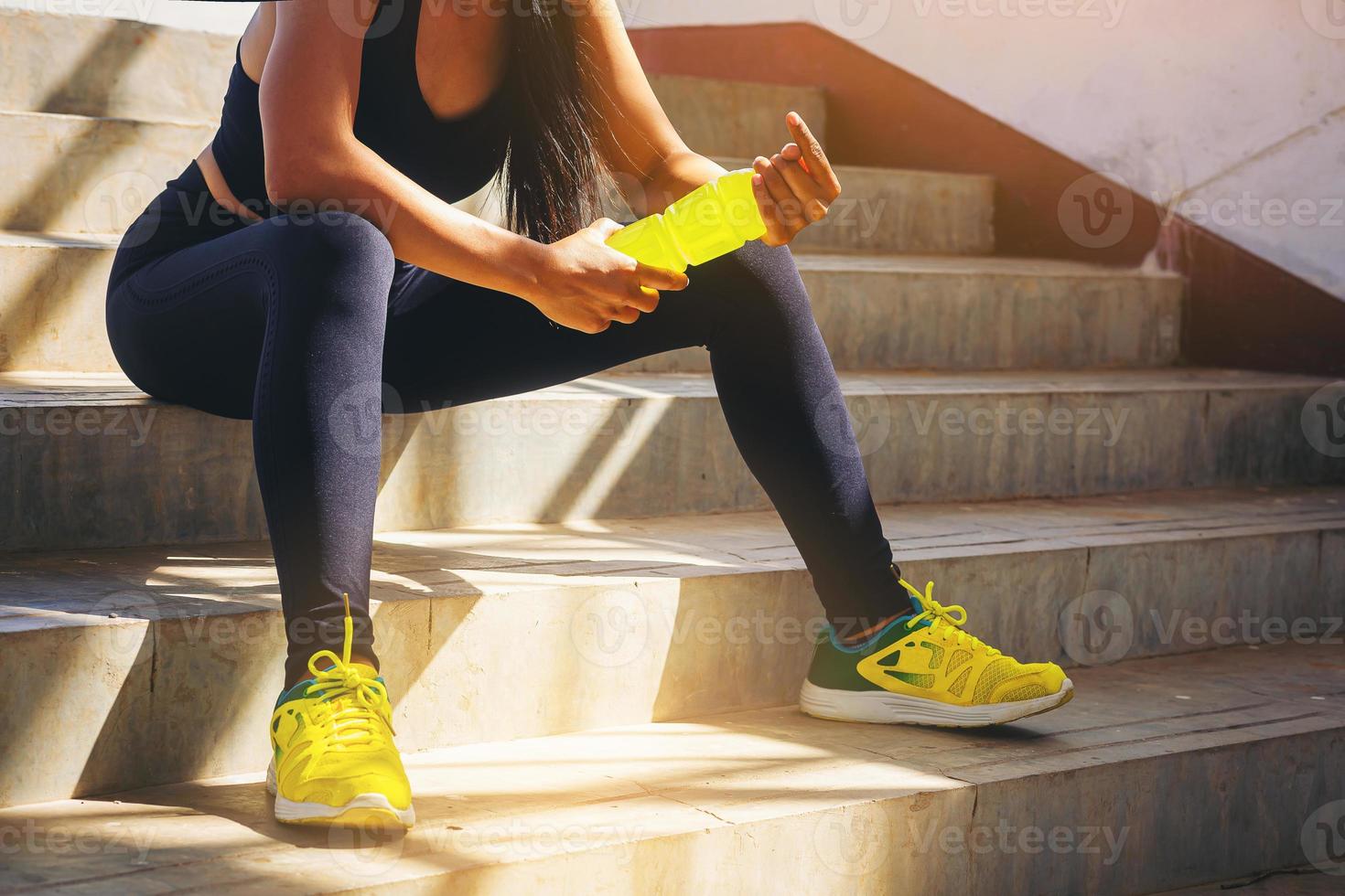 mujer corredora cansada con una botella de electrolito bebe frescura después de entrenar al aire libre en la escalera del estadio. foto