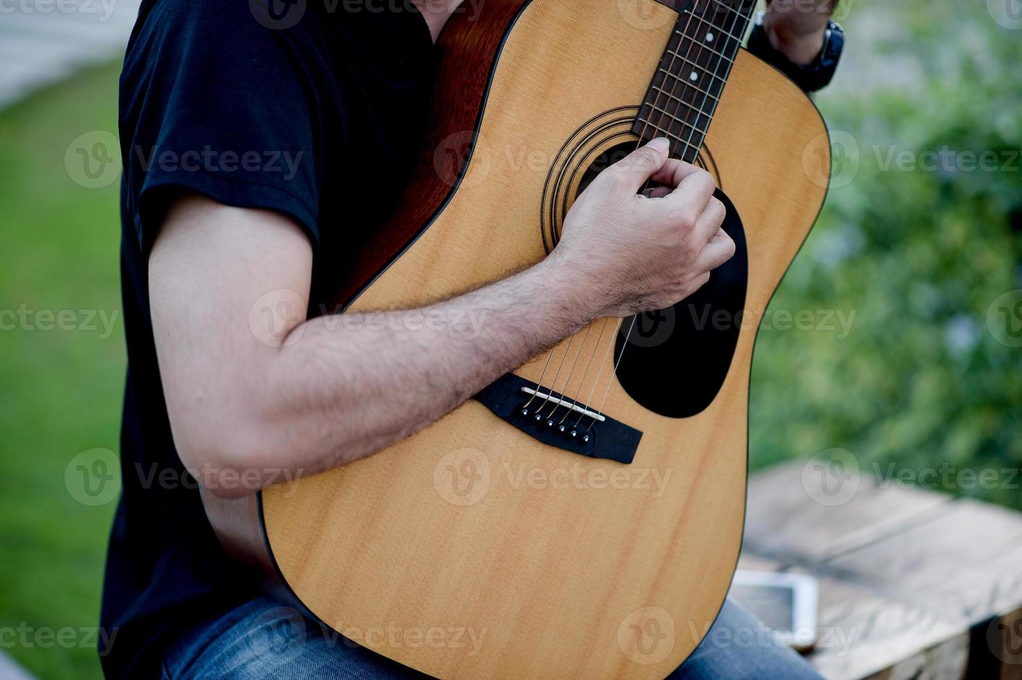 Picture of a guitarist, a young man playing a guitar while sitting in a natural garden,music concept photo
