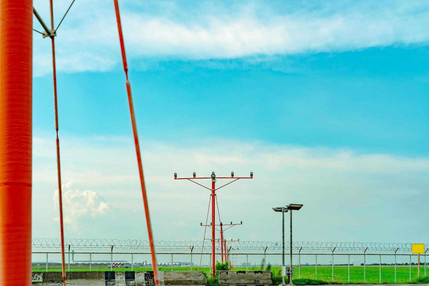 Approach light at the airport. Approach light system concept. Airport runway approach lights. ALS of the airport. Fence for security. Landscape of the airport with green grass field and blue sky. photo