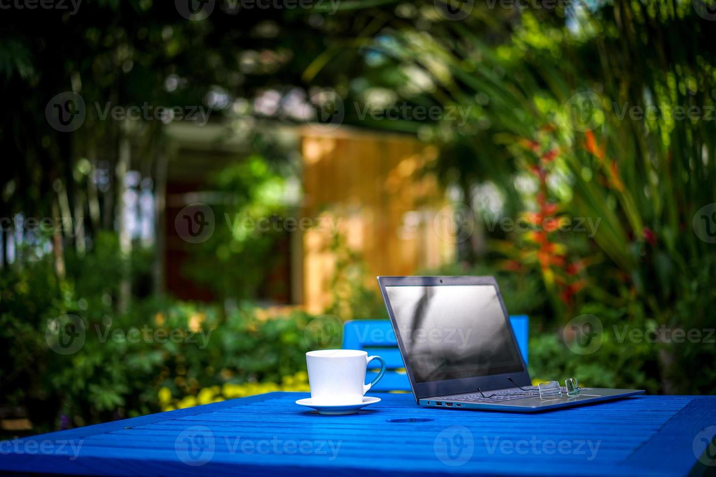 Computer Notebook  Laptop, glasses with the white coffee cup on the dark blue table in the afternoon relaxation time. photo