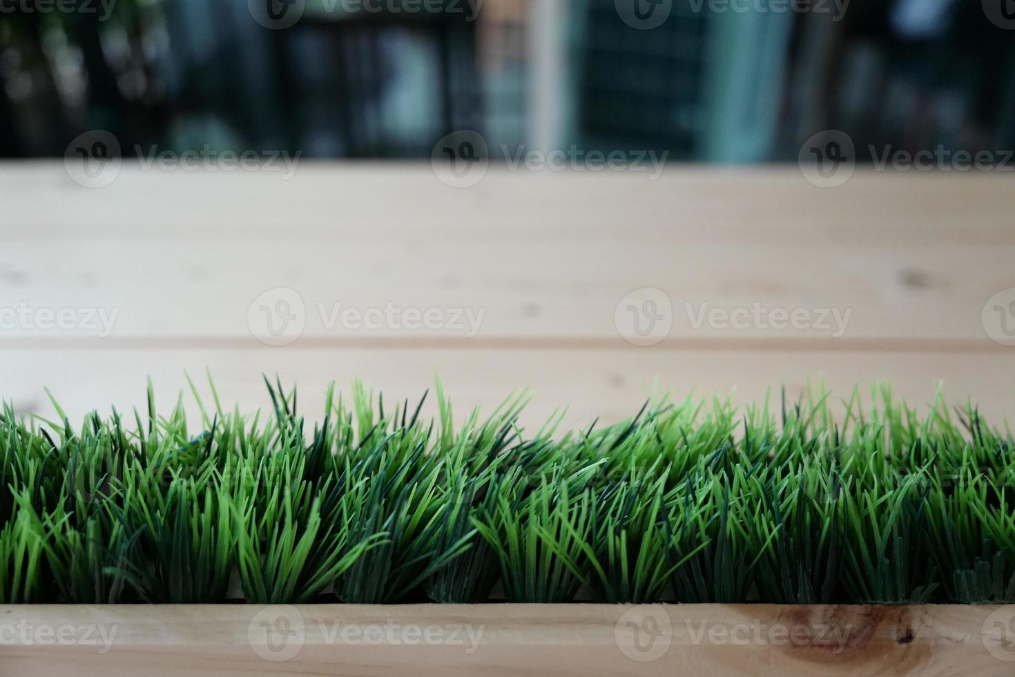 césped verde artificial dispuesto en la fila horizontal en la parte delantera del fondo borroso de la mesa de madera. foto