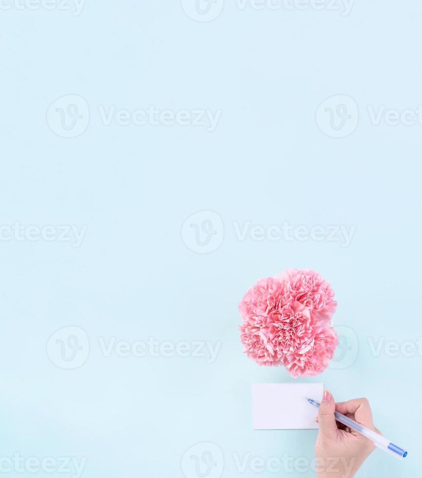 tarjeta de saludo escrita a mano por un joven adolescente aislado con fondo azul pálido, concepto de idea de agradecimiento, deseos, ramo de claveles artesanales, vista superior, espacio de copia, puesta plana, maqueta foto