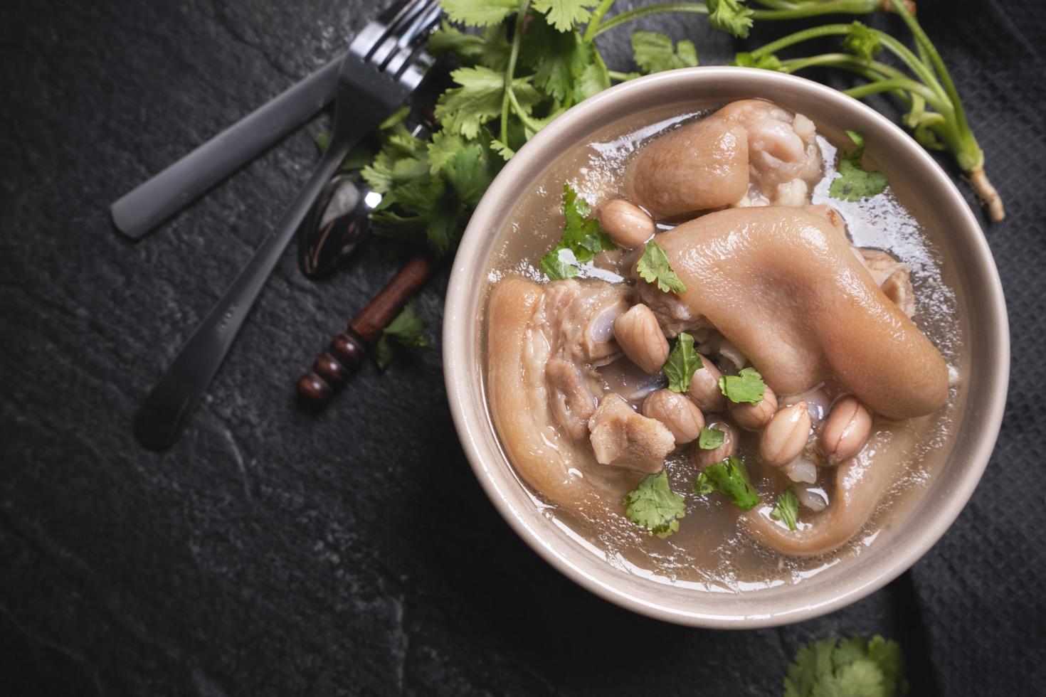 vista superior, primer plano, espacio de copia, comida callejera distintiva asiática de taiwán, sopa de nudillos de cerdo con cacahuate en un tazón de color blanco cremoso marfil beige aislado en una mesa de pizarra de esquisto oscuro foto