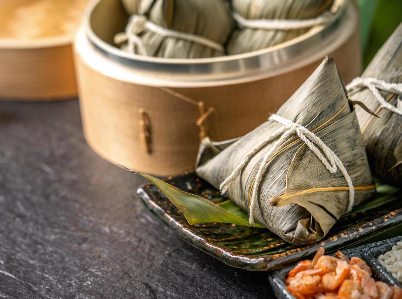 Close up, copy space, famous asian tasty handmade food in dragon boat duan wu festival, fresh from steamer steamed rice dumplings shaped pyramidal wrapped by leaves ingredients photo