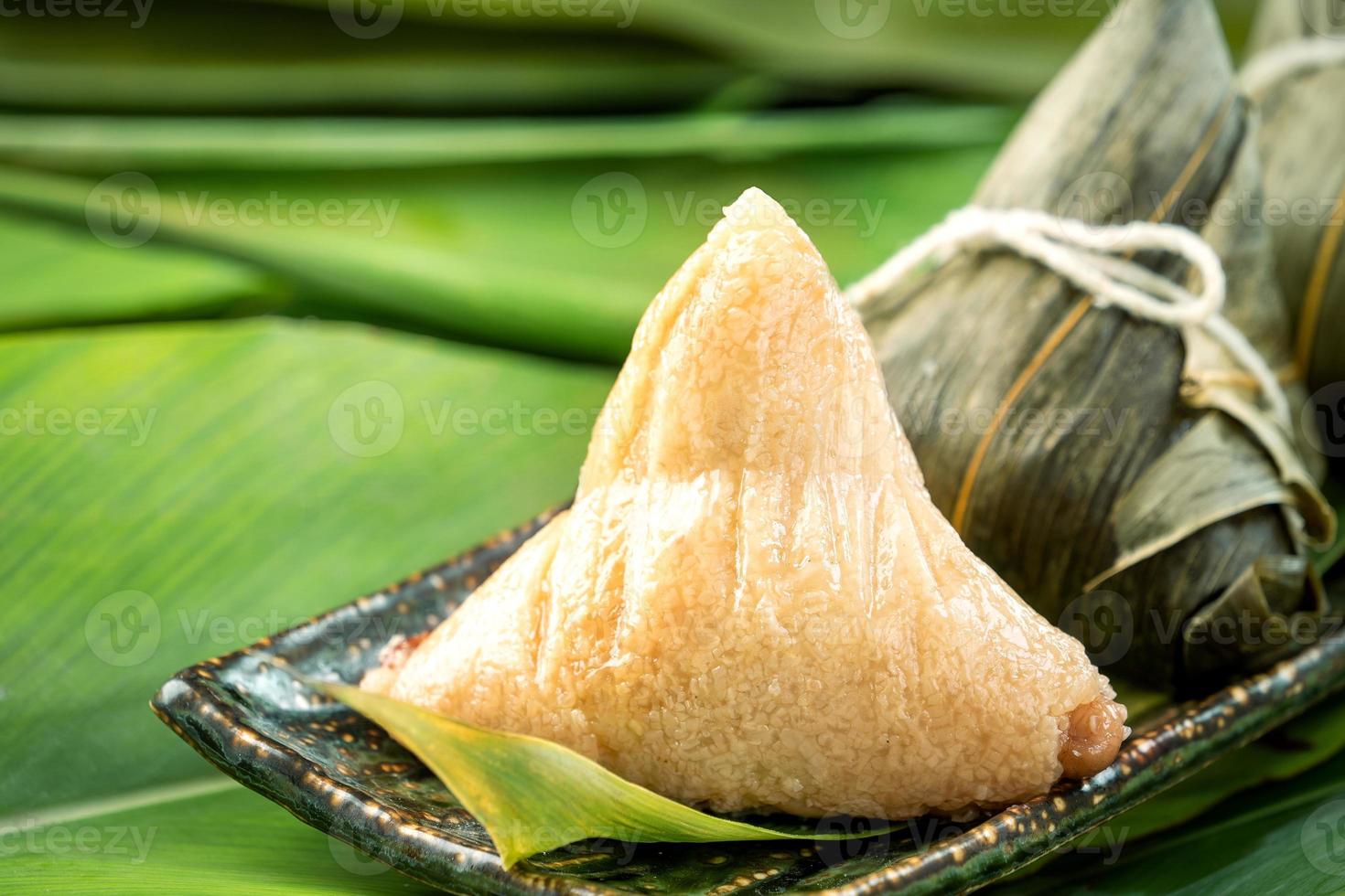 primer plano, espacio de copia, famosa comida china en el festival dragon boat duan wu, albóndigas de arroz al vapor en forma piramidal envueltas en hojas de bambú hechas con ingredientes crudos de arroz pegajoso foto